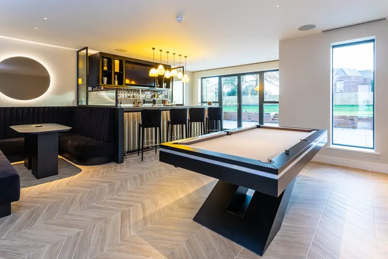 Games room and bar with recessed ceiling lighting, pendant lights over the bar and a lit pool table area
