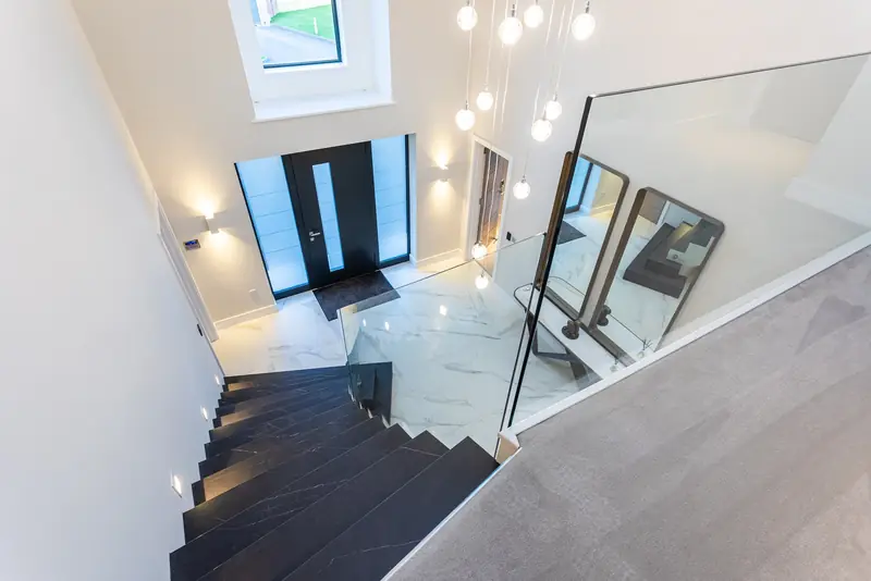 Entrance hall seen from the landing, with a multi-drop pendant light, wall lights and lit stair treads