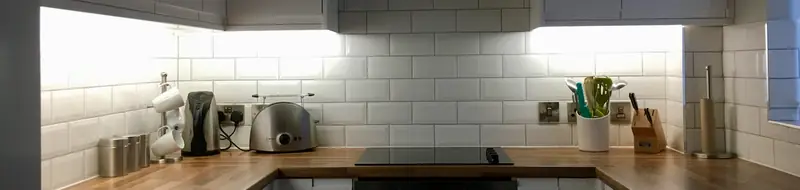 Kitchen worktop lit by under-cupboard lighting above a white metro tile splashback